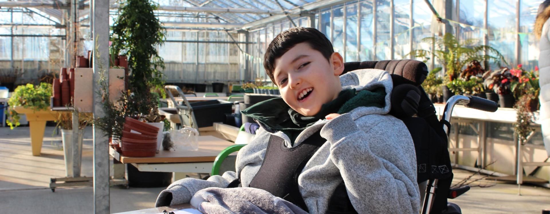 Treloar's primary student in a glasshouse smiling at the camera; plants in the background; a questionnaire on his lap.