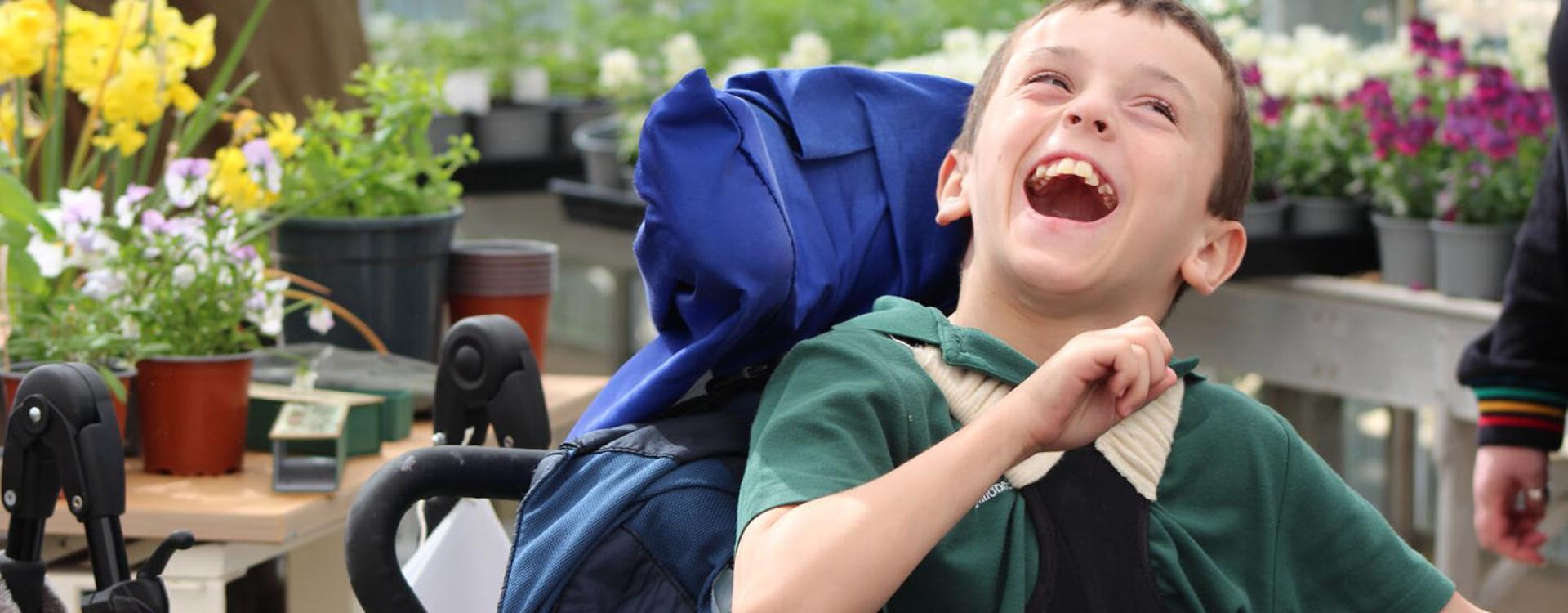 Treloar's student laughing; he is in the greenhouse; plants and flowers in the background.