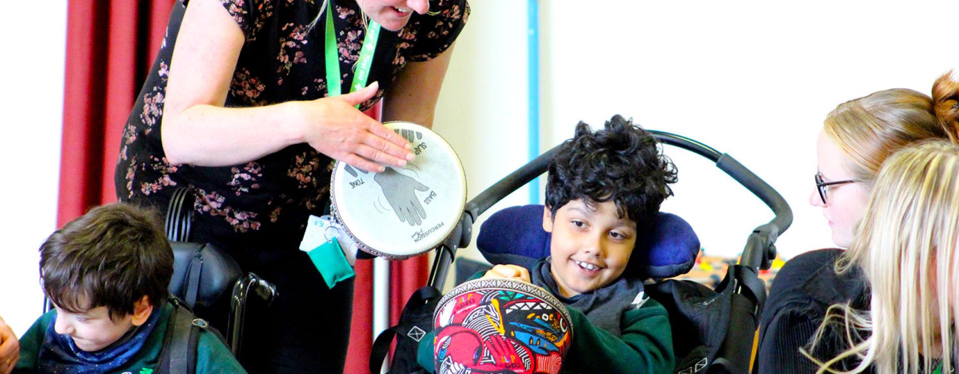 Treloar's student holding an African drum and tapping it; he looks happy. He is surrounded by Treloar's staff.