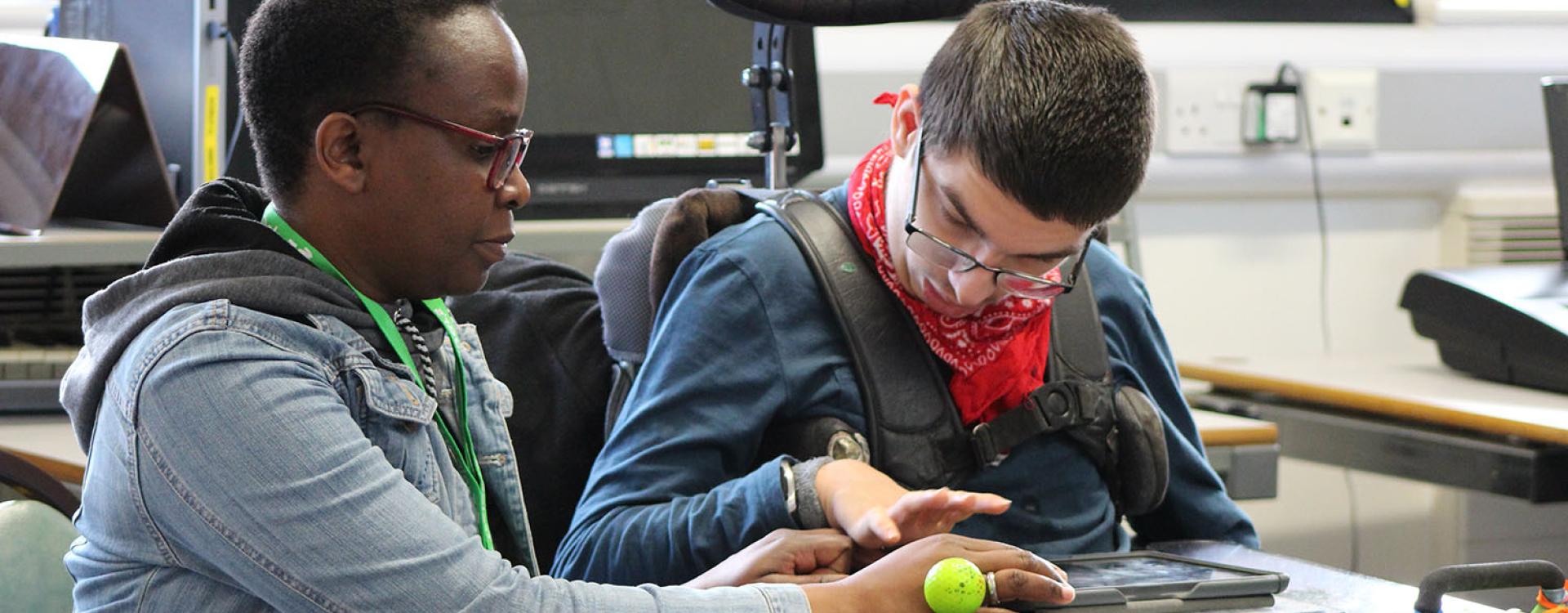 Treloar College using his iPad to play clarion; his assistant is helping him by supporting his hand.