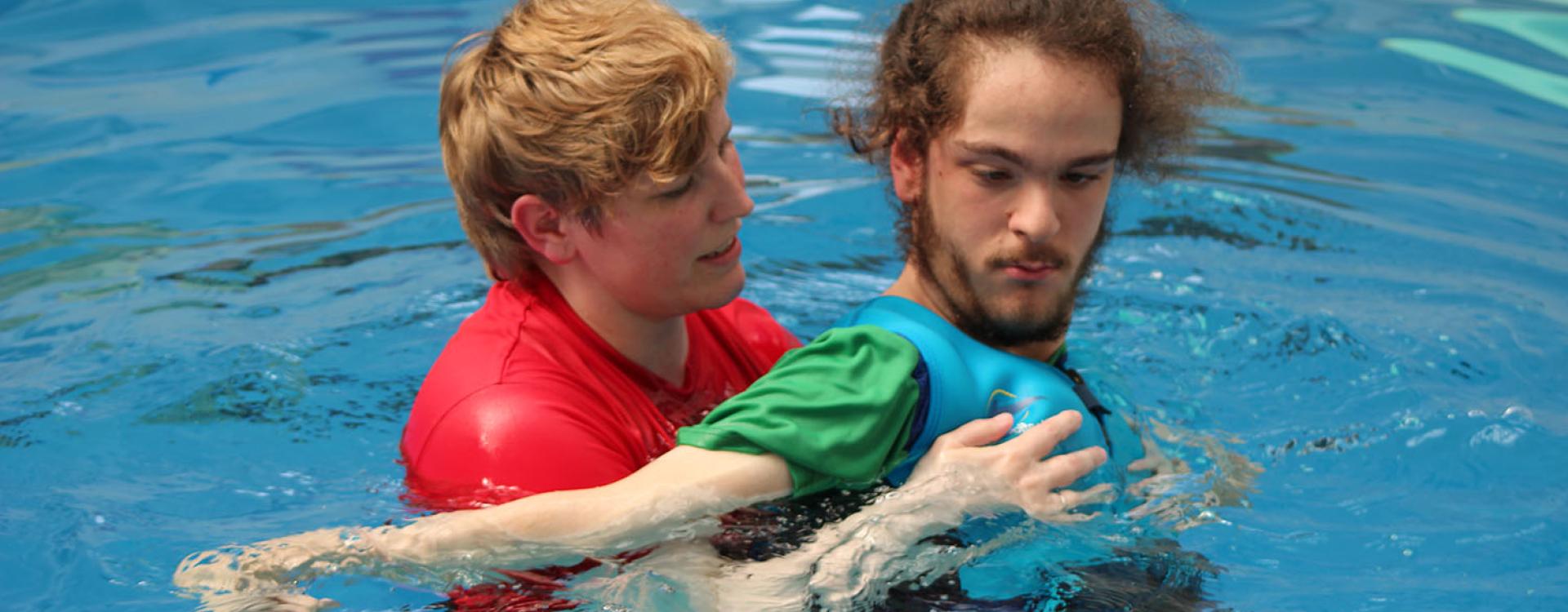 Treloar College student in the pool with his assistant who is holding him and helping him swim.