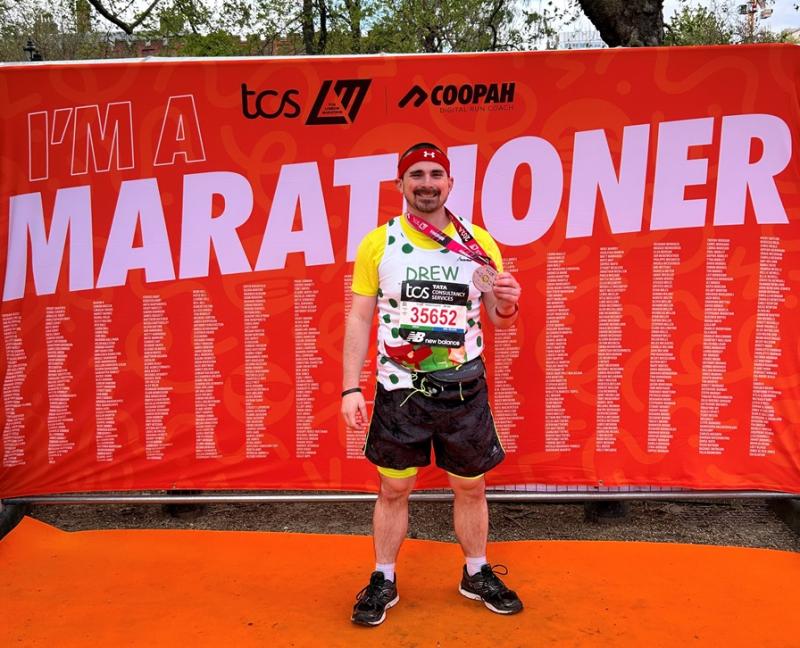 Treloar's supporter Andrew posing for a photo after the marathon; a big red banner saying 'marathoner' behind him.