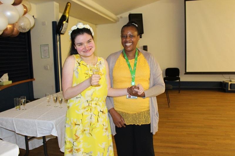 Treloar College student with her assistant, wearing a yellow dress and holding a glass, photographed during her prom. 