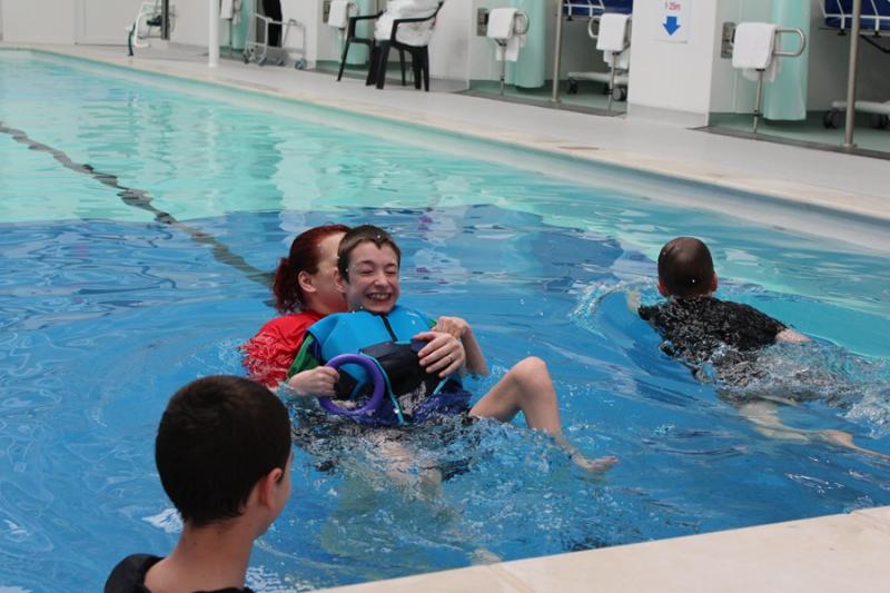 Day of Disability Sports at Treloar's: students in the pool; Treloar's student in on his back, being held by his assistant and she is helping him swim - he is using his legs.