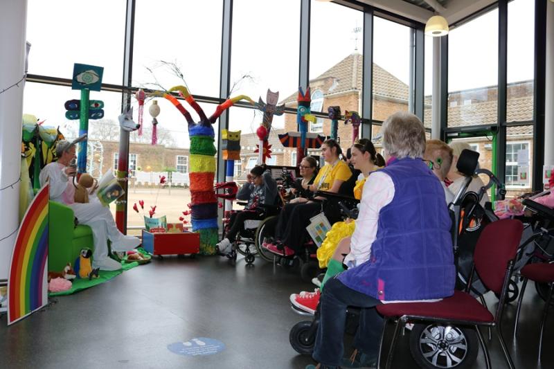 Story reading in the Jowette Centre: a group of students with their assistants sitting in semi circle, listening to a staff member reading a book.