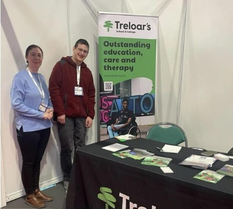 Maria Sherwood, Treloar's Progress and Transition Team Manager at Naidex with former student Eoin standing by Treloar's exhibition stand with branded merchandise.