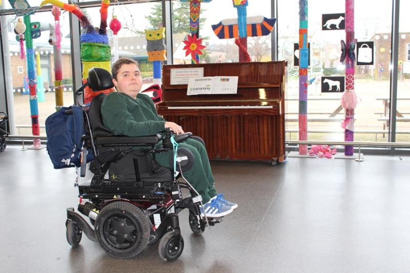 College student Thomas posing for a photo in the Jowett centre; in the background a floor-to-ceiling window and student-made sculptures and a piano.