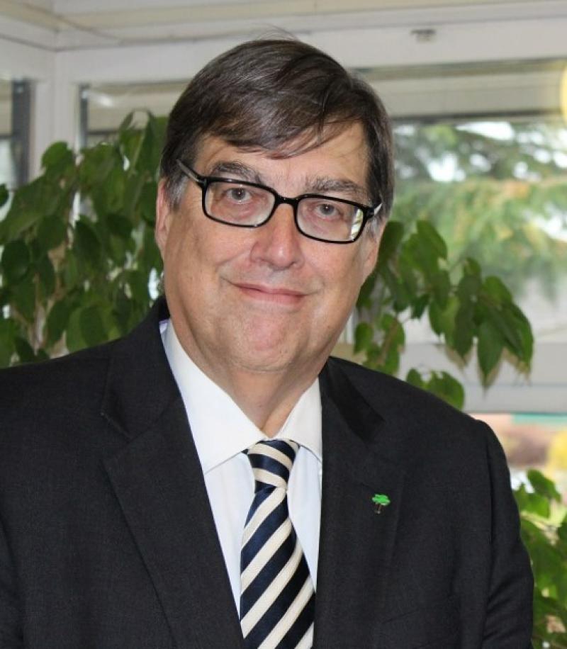 Tony Reid wearing a black suit, a white shirt and a black and white stripey tie.