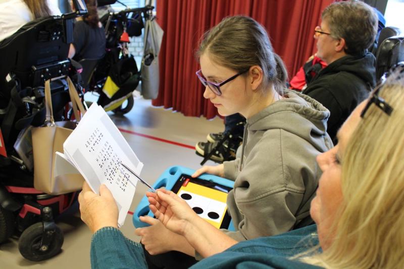 In assembly, Treloar School student is looking at a braille book together with her support assistant.