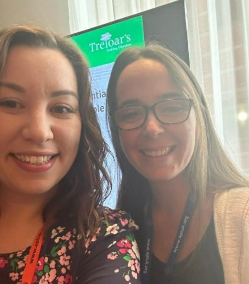 Claire taking a selfie with a woman  at the conference; A screen with a presentation about Treloar's in the background.