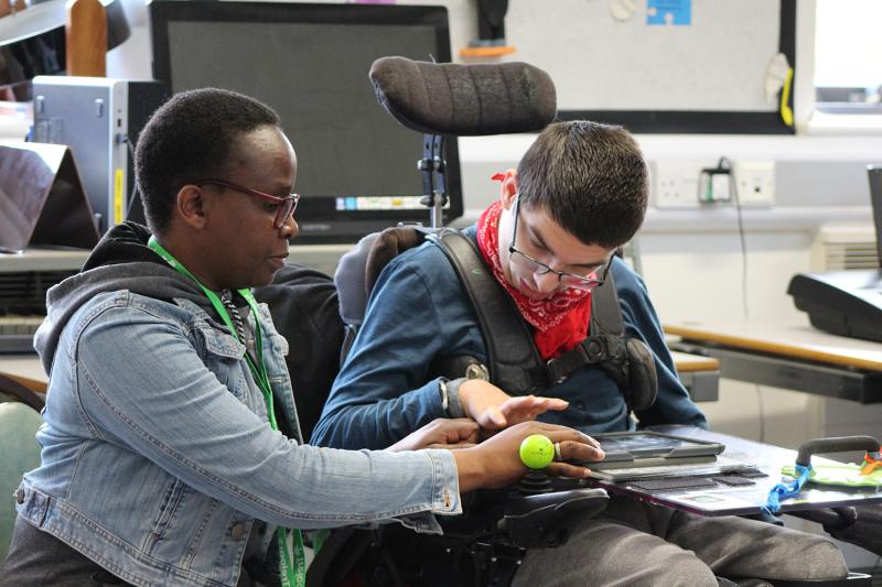 Treloar College using his iPad to play clarion; his assistant is helping him by supporting his hand.