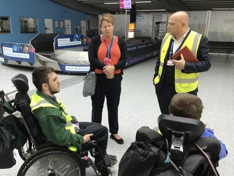 2 Treloar College students at Southampton Airport during their internship. They are talking to 2 members of staff and are located in the baggage reclaim area by the belts.