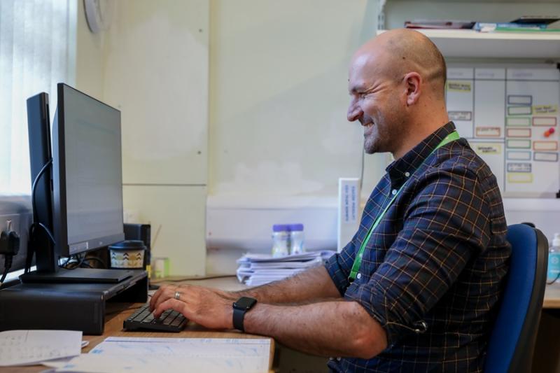 Treloar's member of staff at his desk; he is smiling and using his PC.