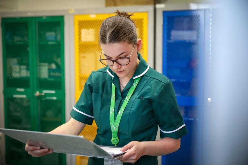 Treloar's Medicine Management Technician is holding a big medical chart in her handing and carefully looking at it; she is wearing a dark green uniform.