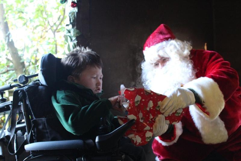 Treloar's primary student unwrapping a Christmas present gifted to him by Santa. Santa is helping him unwrap the gift wrapped in red wrapping paper.