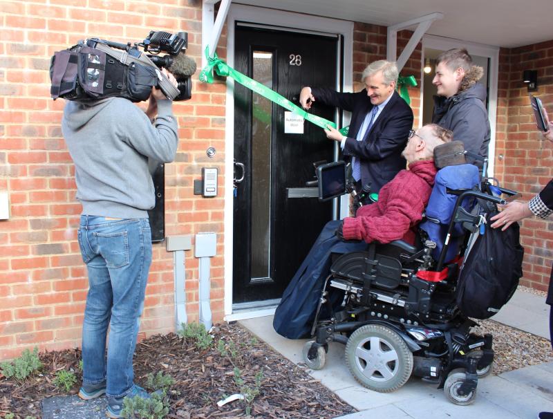 MP Damian Hinds cutting a green Treloar's ribbon to formally open the Rivermead Gardens flats, alongside two of the first residents Eoin and Kane.