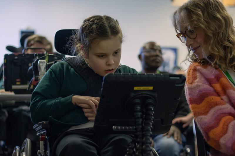 Treloar School student looking at her iPad and her assistant is leaning over to see what see is working on.