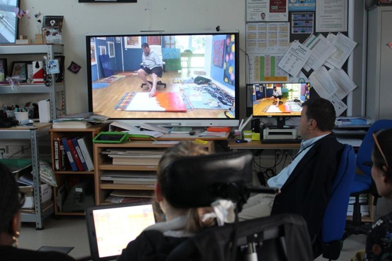 Treloar's patron Tom Yendell, a mouth and foot painter, talking to Treloar's students in a classroom, sharing a video showing him painting using his foot.