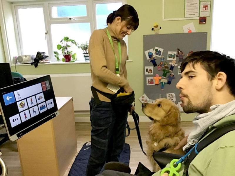 Treloar College student used his AAC device during his work experience to communicate a command to Stanley 'sit'; the dog is sitting and waiting for a treat from his trainer.