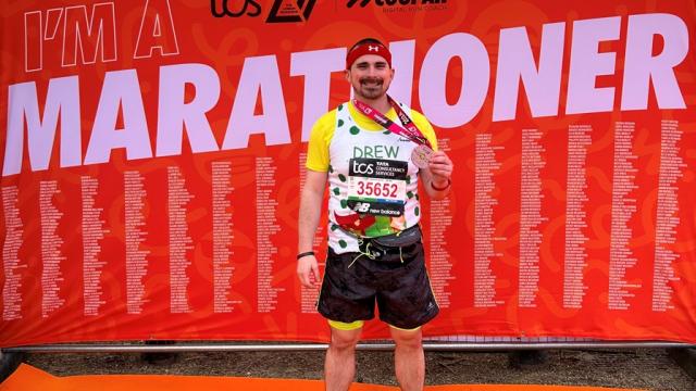 Treloar's supporter Andrew posing for a photo after the marathon; a big red banner saying 'marathoner' behind him.