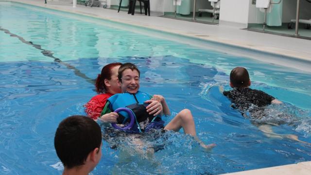 Day of Disability Sports at Treloar's: students in the pool; Treloar's student in on his back, being held by his assistant and she is helping him swim - he is using his legs.