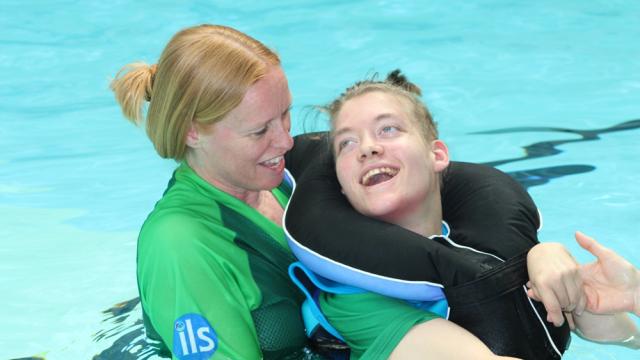 Treloar's student in the pool with her support assistant; the student is in the pool, being held by her assistant. Both are smiling at each other and having a good time.