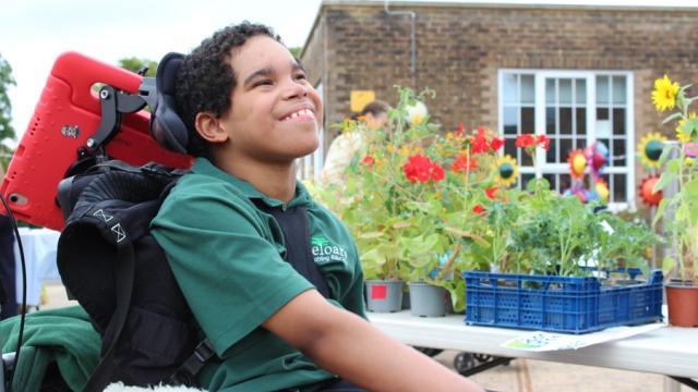 Treloar's student with a smile on his face: he is looking up into the sky; there are pots with flowers in the background.