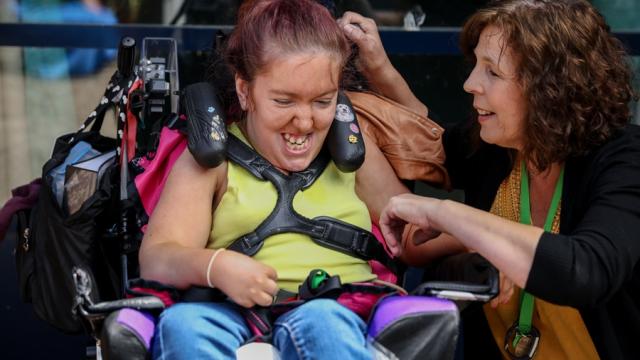 Treloar's student laughing and her assistant is kneeling next to her and talking to her.