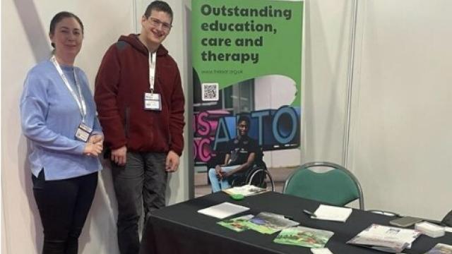 Maria Sherwood, Treloar's Progress and Transition Team Manager at Naidex with former student Eoin standing by Treloar's exhibition stand with branded merchandise.