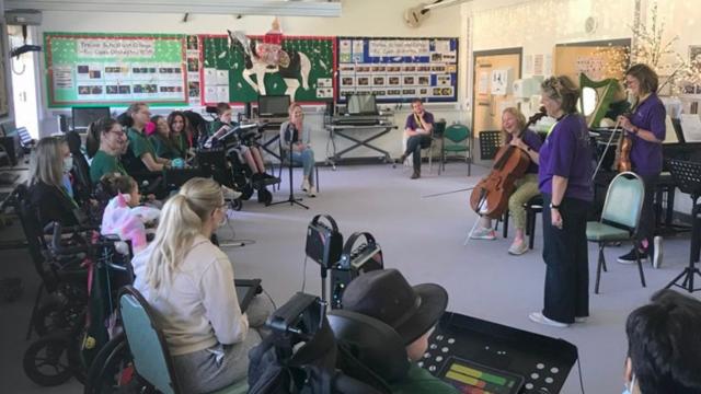 Jenny and Judith from the Bournemouth Symphony Orchestra, led a workshop with Treloar's students in a music classroom. Students and staff sitting in a semi-circle and the musicians are standing in front of the group