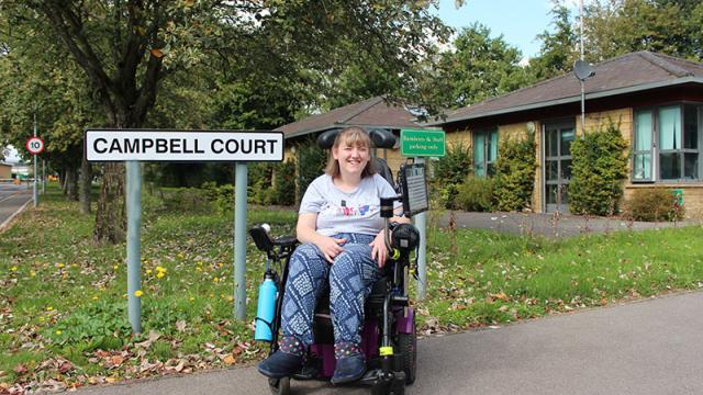 Campbell Court resident posing out the court, but the sign 'Campbell Court'.