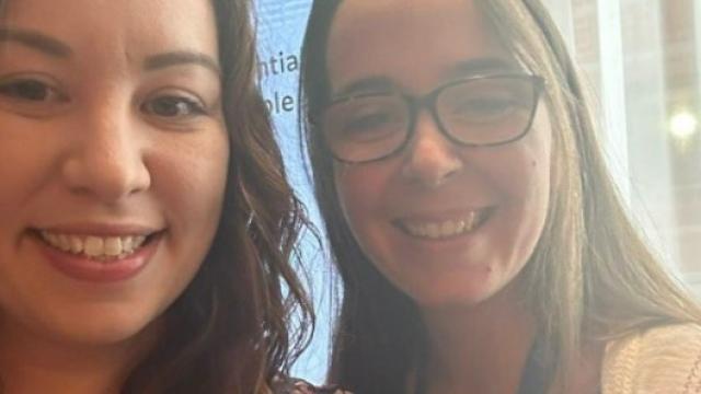 Claire taking a selfie with a woman  at the conference; A screen with a presentation about Treloar's in the background.