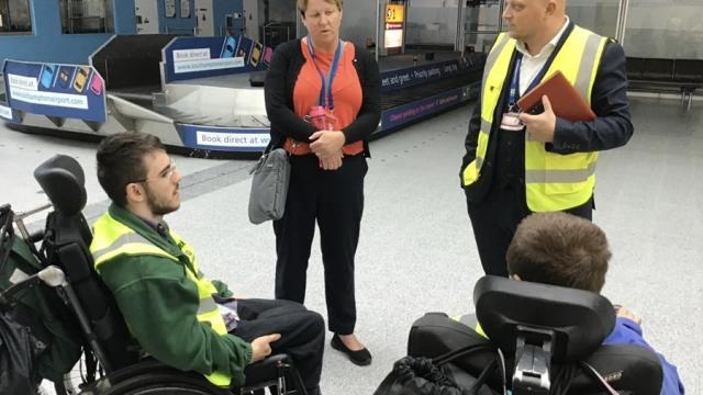 2 Treloar College students at Southampton Airport during their internship. They are talking to 2 members of staff and are located in the baggage reclaim area by the belts.