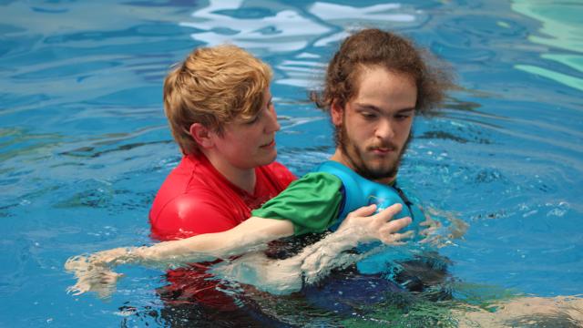 Treloar College student in the pool with his assistant who is holding him and helping him swim.