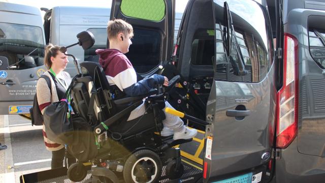 Treloar College student using a lift to get into a minibus and his assistant is standing next to the vehicle, holding the remote which controls the lift.