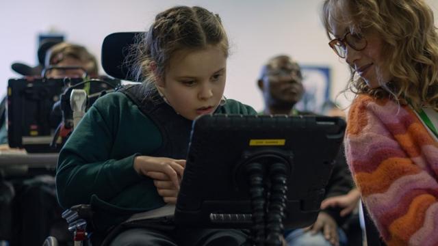 Treloar School student looking at her iPad and her assistant is leaning over to see what see is working on.