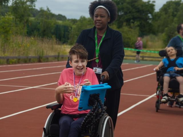 Treloar's student is on the athletic track and her assistant is pushing the wheelchair.