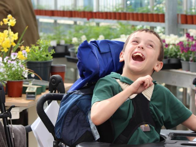 Treloar's student laughing; he is in the greenhouse; plants and flowers in the background.