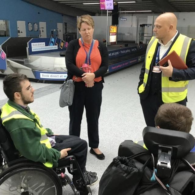 2 Treloar College students at Southampton Airport during their internship. They are talking to 2 members of staff and are located in the baggage reclaim area by the belts.