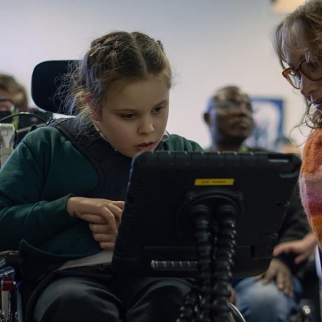 Treloar School student looking at her iPad and her assistant is leaning over to see what see is working on.