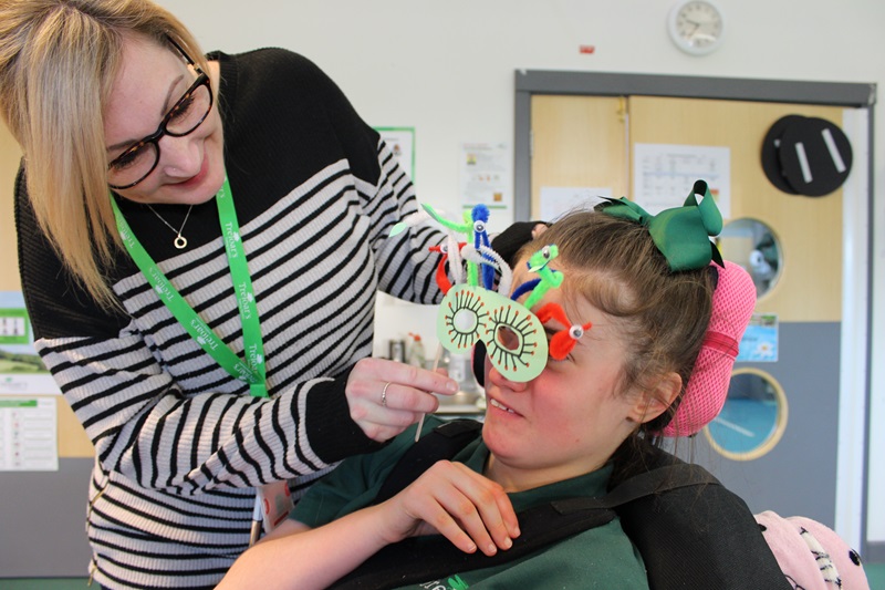 KS3 student with her assistant during KS3 topic launch 'Mythical creatures'; the assistant is holding a 'Medusa' mask in front of the student's face