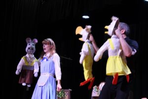 2 performers from Box Tale Soup on stage at Treloar's during their Alice in Wonderland show: the female performer is wear a light blue dress and holding a rabbit puppet; the male performer is holding 2 bird puppets