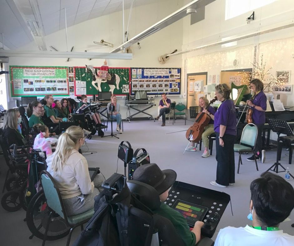 Jenny and Judith from the Bournemouth Symphony Orchestra, led a workshop with Treloar's students in a music classroom. Students and staff sitting in a semi-circle and the musicians are standing in front of the group