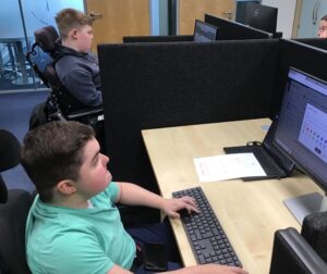 2 Treloar College students at their desks in front of PCs, during their work experience at a pharmaceutical company Aspire.